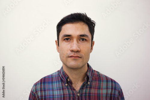 Male mugshot for passport. Serious portrait of adult man for id card. Visa picture. Soft focus. Film grain texture. Korean guy taking picture for papers in studio against white wall. 