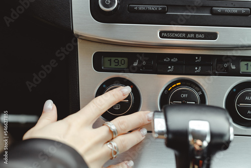 Woman turning button of air conditioning regulating temperature in car