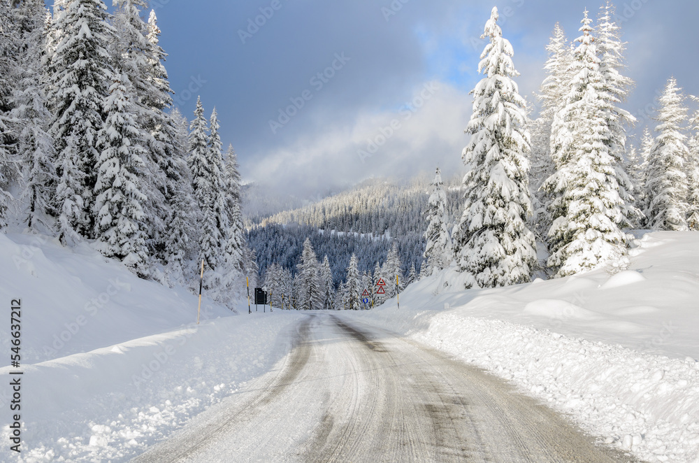Deserted icy road through a snowy forest in the mountains on a sunny winter day Deserted icy road through a snowy forest in the mountains on a sunny winter day