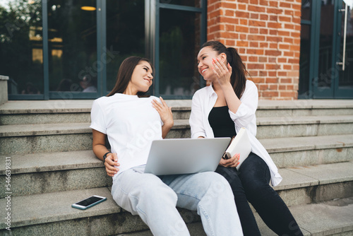Young woman with laptop in conversation with friend on steps