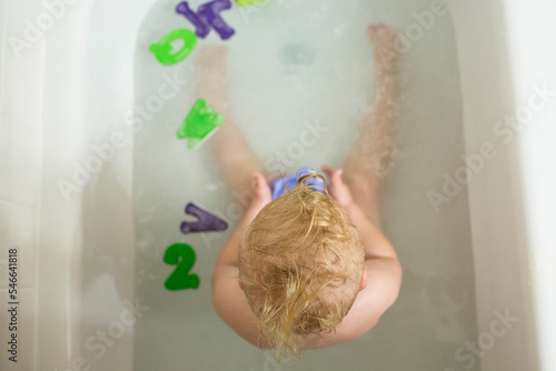 Overhead view of naked boy playing with toys in bathtub at home photo