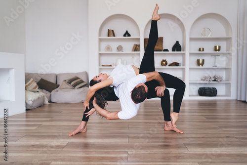 Flexible woman doing acro yoga with instructor in room