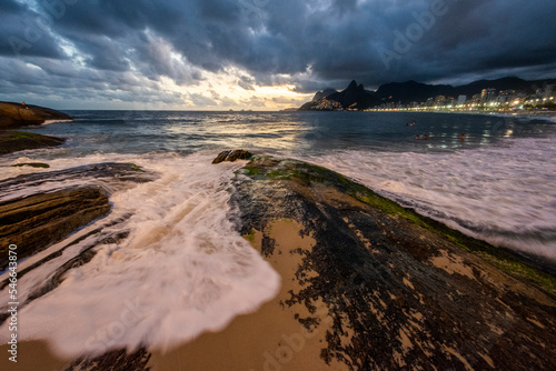 Landscape of wave splashing on rock in Ipanema Beach during sunset photo