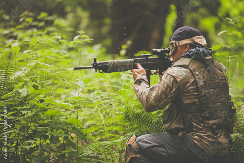 A man aims an automatic weapon while in a lush forest. photo