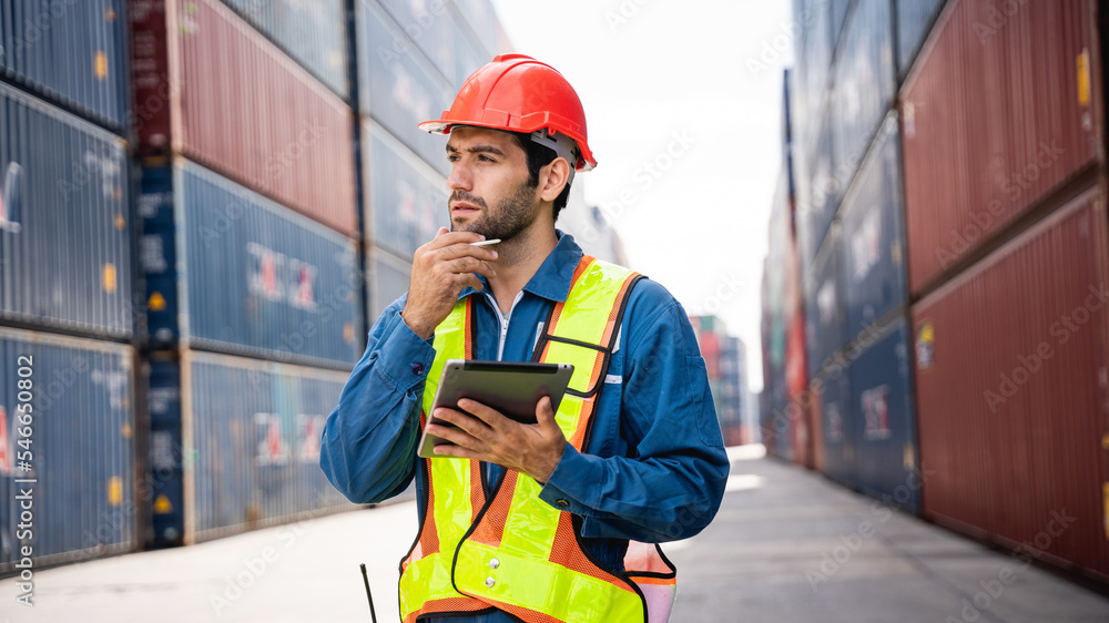 Engineer or foreman checking inventory or task details at container yard warehouse while wearing PPE and holding tablet., Logistics concept inside the shipping, import, and export industries. Engineer or foreman checking inventory or task details at container yard warehouse while wearing PPE and holding tablet., Logistics concept inside the shipping, import, and export industries.