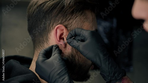 Tattoo piercing studio - a woman makes an ear piercing to a man to a guy