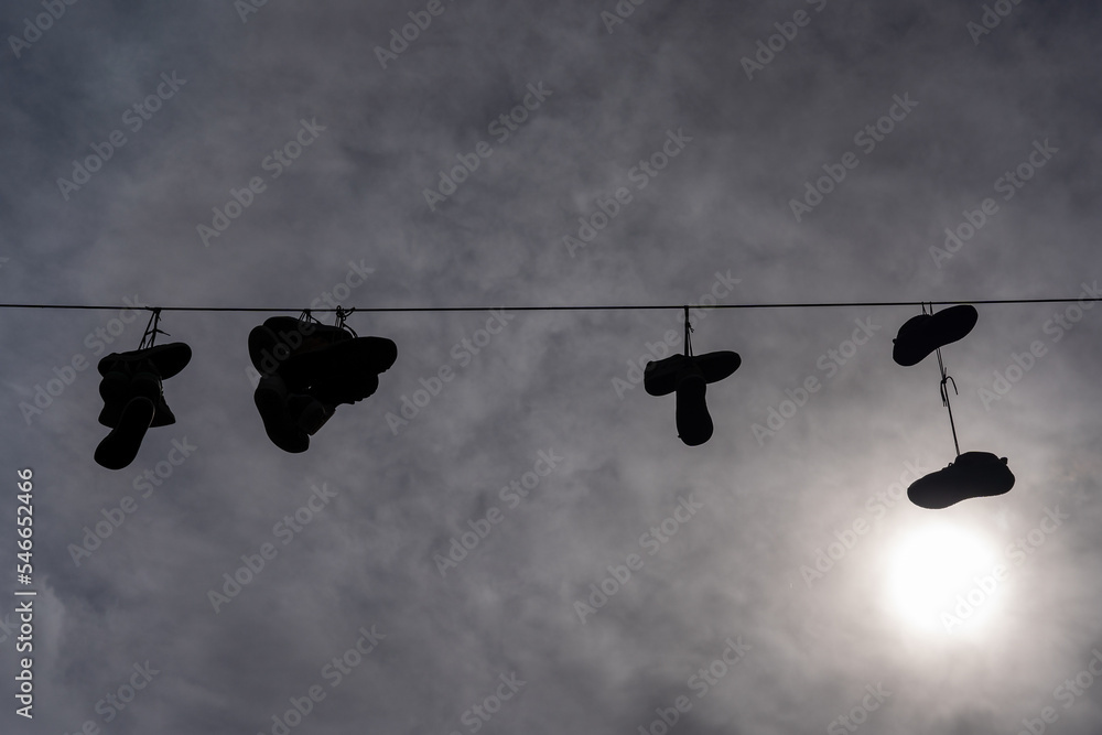 a dramatic sky with white clouds behind which is the sun, but a black rope is stretched across it, on which a few pairs of shoes are hanging a dramatic sky with white clouds behind which is the sun, but a black rope is stretched across it, on which a few pairs of shoes are hanging