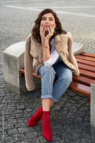 Obraz na płótnie Beautiful young woman wearing teddy jacket jeans and white shirt sitting on a bench in the city w salonie