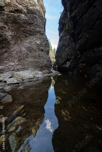 a dark rocky valley in Norway, Helvete, where between rocky gray rocks there is water reflecting the blue sky and some green bushes