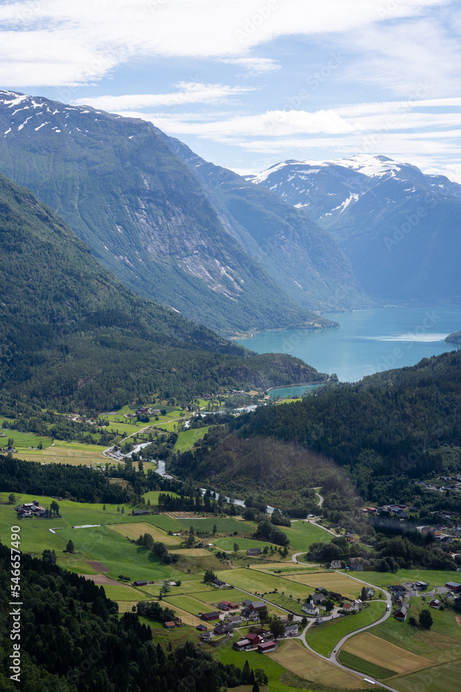 Norwegian mountain landscape from a high mountain down in the valley there is a village and in the distance between the mountain you can see a fjord with blue water above which there is beautiful sky