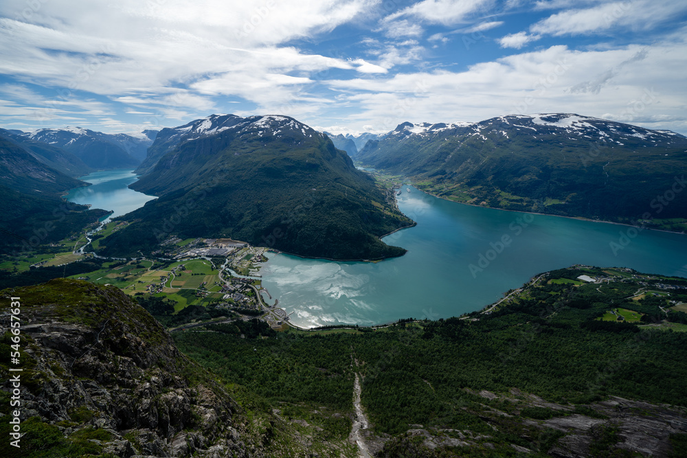 Norwegian mountain landscape from a high mountain down in the valley there is a village and in the distance between the mountain you can see a fjord with blue water above which there is a beautiful 