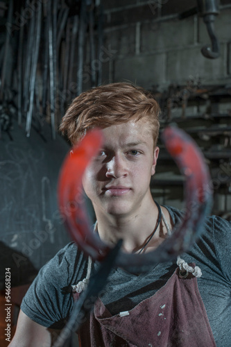 Apprentice blacksmith with hammered red hot horseshoe at workshop