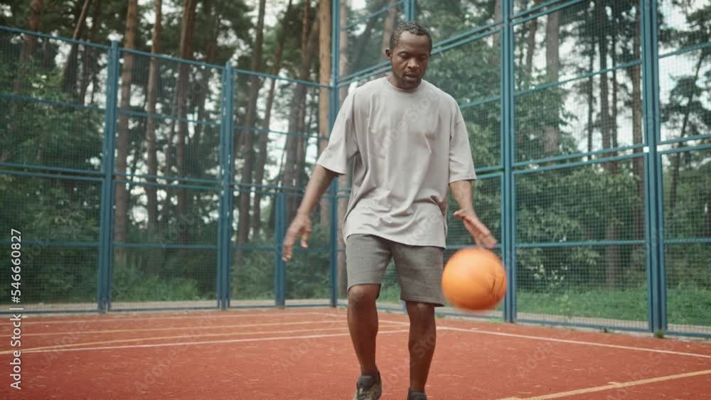 African American mature guy playing basketball bouncing ball and moving on playground. One adult man in sportswear running on urban court practicing basketball moves outdoors. Sport lifestyle African American mature guy playing basketball bouncing ball and moving on playground. One adult man in sportswear running on urban court practicing basketball moves outdoors. Sport lifestyle