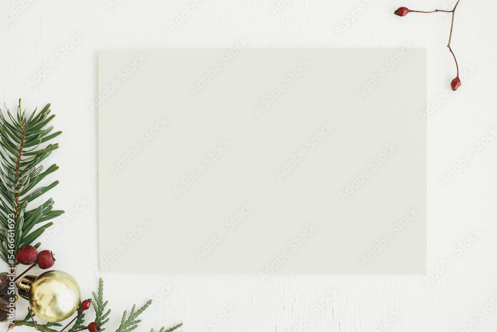Christmas card flat lay. Empty greeting card mock up and fir branches, berries and christmas decorations on rustic white table. Postcard template with space for text. Happy Holidays!