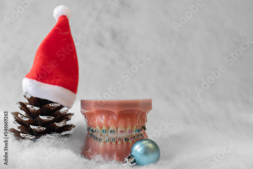  Lustiger zahnärztlicher Weihnachtshintergrund mit Platzhalter. Zahnmodell mit festsitzender Zahnspange trägt eine Weihnachtsmütze und isst eine Weihnachtskuge