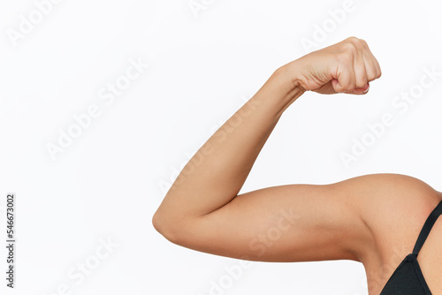 Bild auf Leinwand Cropped shot of young tanned strong fit woman raising arm and showing bicep on a white background