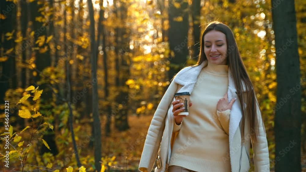 Dreamy brunette woman in white jacket walks carefully looking down. Smiling lady having a walk by the autumn park with a cup of coffee. Dreamy brunette woman in white jacket walks carefully looking down. Smiling lady having a walk by the autumn park with a cup of coffee.