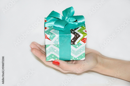 Fototapeta Naklejka Na Ścianę i Meble -  a box with a gift for a holiday or celebration in a female hand on an open palm on a white background. congratulations on the new year, christmas, birthday or other celebrations and memorable events