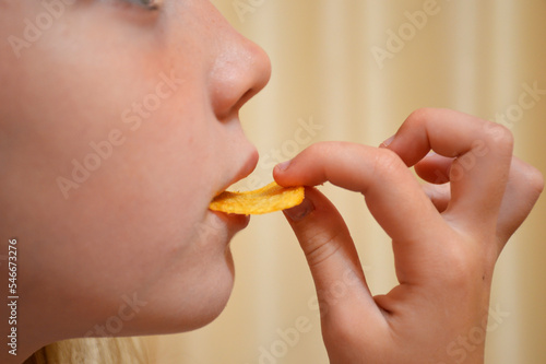 a large palan girl bites potato chips holding them with her lips and hands. fast food is harmful and unhealthy food for a young body. carcinogens and fats