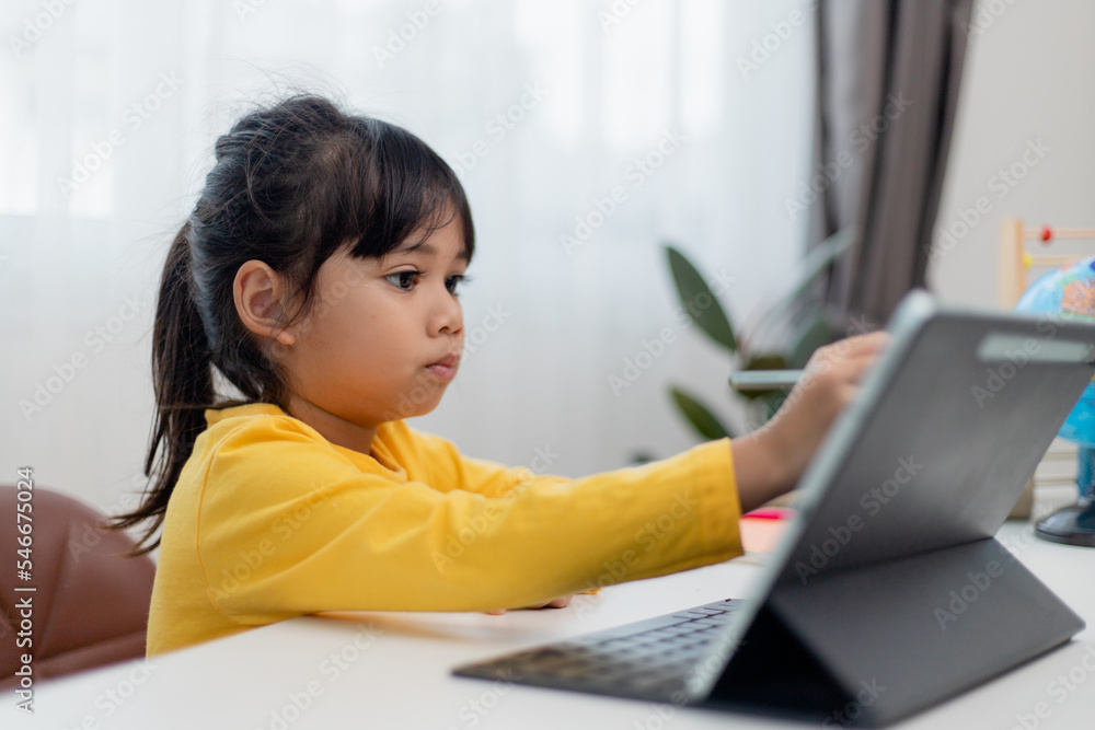 Asian schoolgirl doing her homework with digital tablet at home. Children use gadgets to study. Education and distance learning for kids. Homeschooling during quarantine. Stay at home Asian schoolgirl doing her homework with digital tablet at home. Children use gadgets to study. Education and distance learning for kids. Homeschooling during quarantine. Stay at home