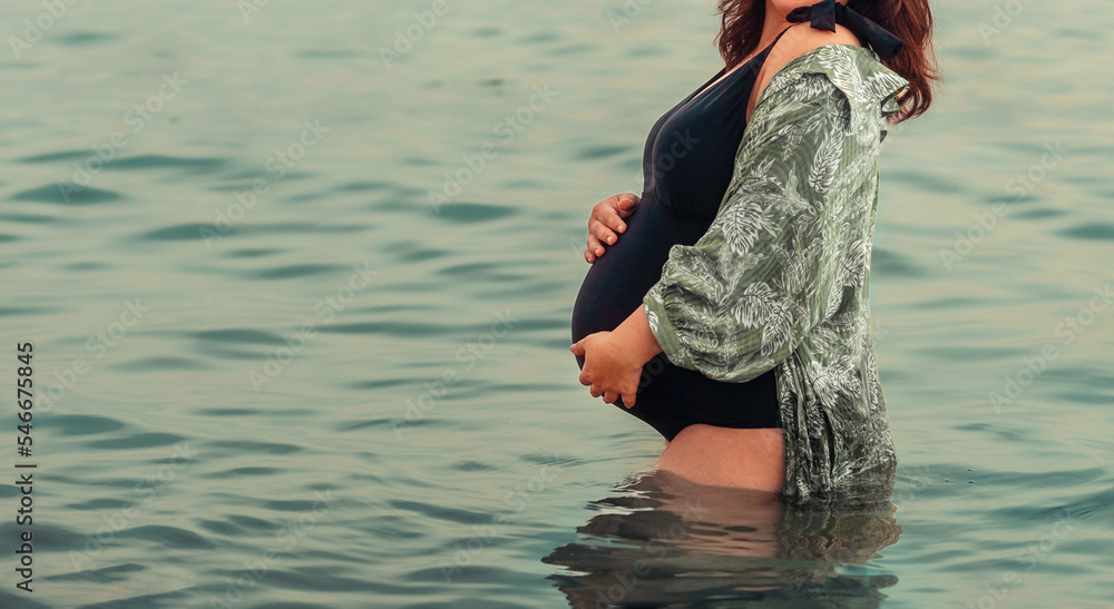 Motherhood and pregnancy. Young pregnant woman in swimsuit is standing