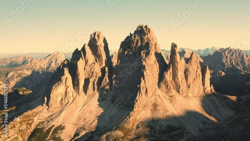 Lit by rising sun battlement-like peaks of rocky mountains. Wide canyons covered with shadows under clear sky. Tre Cime di Lavaredo at sunrise aerial view photo