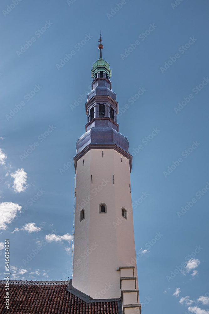 Estonia, Tallinn - July 21, 2022: Closeup of white bell tower with gray topsection ending in golden pinnacle of Holy Spirit Church against blue cloudscape