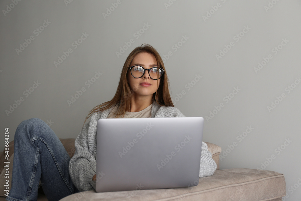 Close up shot of young smiling woman working remotely from home on laptop, sitting on the couch in living room. Female freelancer in blue light glasses with hands on keyboard. Copy space, background. Close up shot of young smiling woman working remotely from home on laptop, sitting on the couch in living room. Female freelancer in blue light glasses with hands on keyboard. Copy space, background.