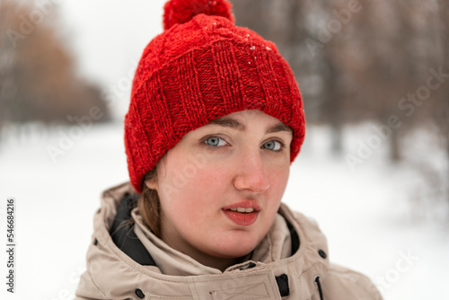 Beautiful young woman stare in camera, red knitted hat and mittens. Face of woman in knitted headdress in winter park