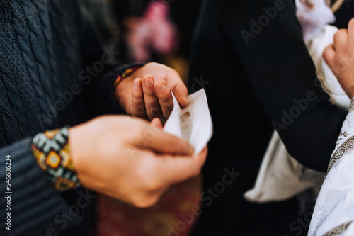 A man, dad, godfather holds a paper with the hair of a newborn child in his hands after the haircut ceremony in the church. Photography, religion.