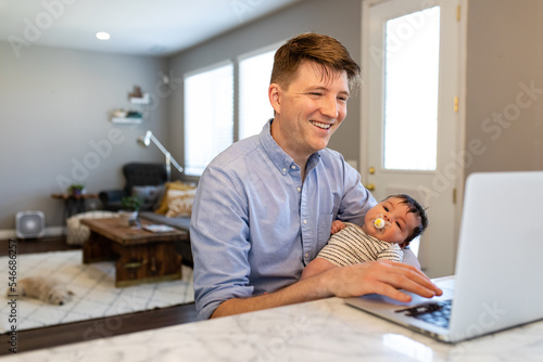 Man Mutiltasks Working On Laptop While Holding A Baby photo