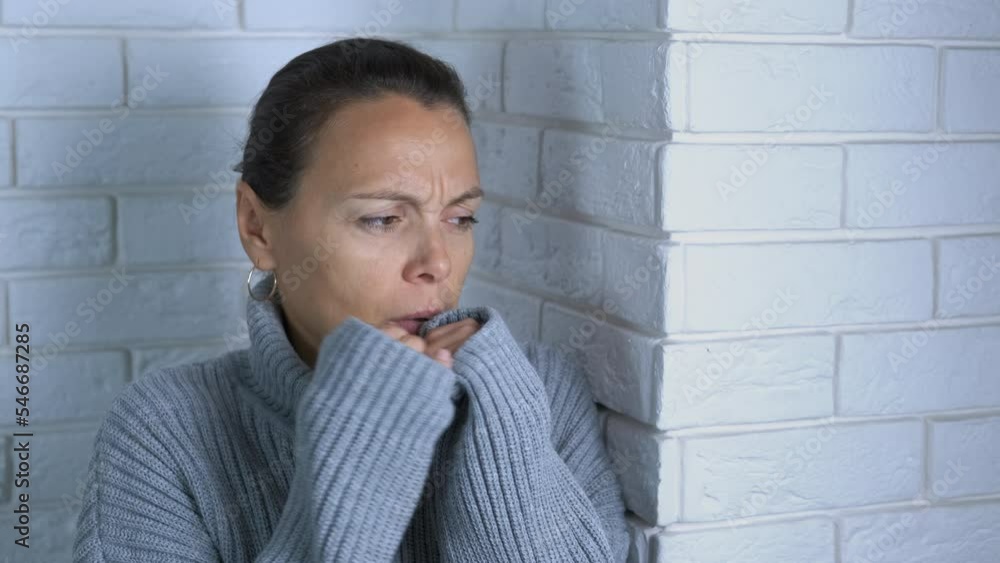 Room heating problem. A sad female wraps herself in a warm sweater and looks out the window. Room heating problem. A sad female wraps herself in a warm sweater and looks out the window.
