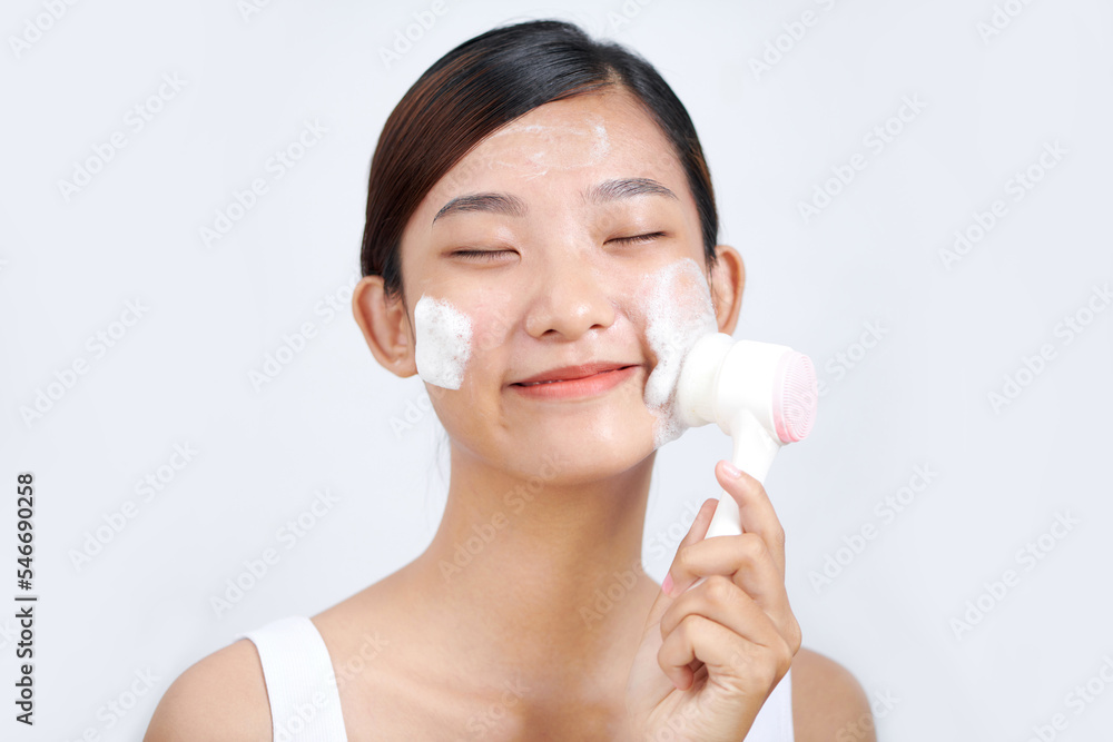 The girl cleans the skin of the face with a brush and foam for washing The girl cleans the skin of the face with a brush and foam for washing