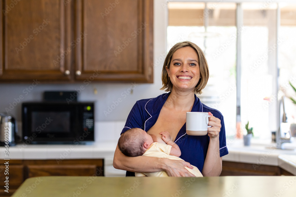 Mother Enjoys A Cup Of Tea While Nursing Her Newborn In The Kitchen Mother Enjoys A Cup Of Tea While Nursing Her Newborn In The Kitchen