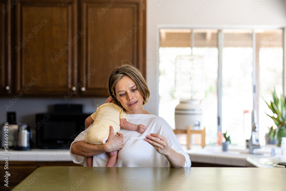 Woman Looks At The Temperature On A Thermometer While Holding Infant Woman Looks At The Temperature On A Thermometer While Holding Infant