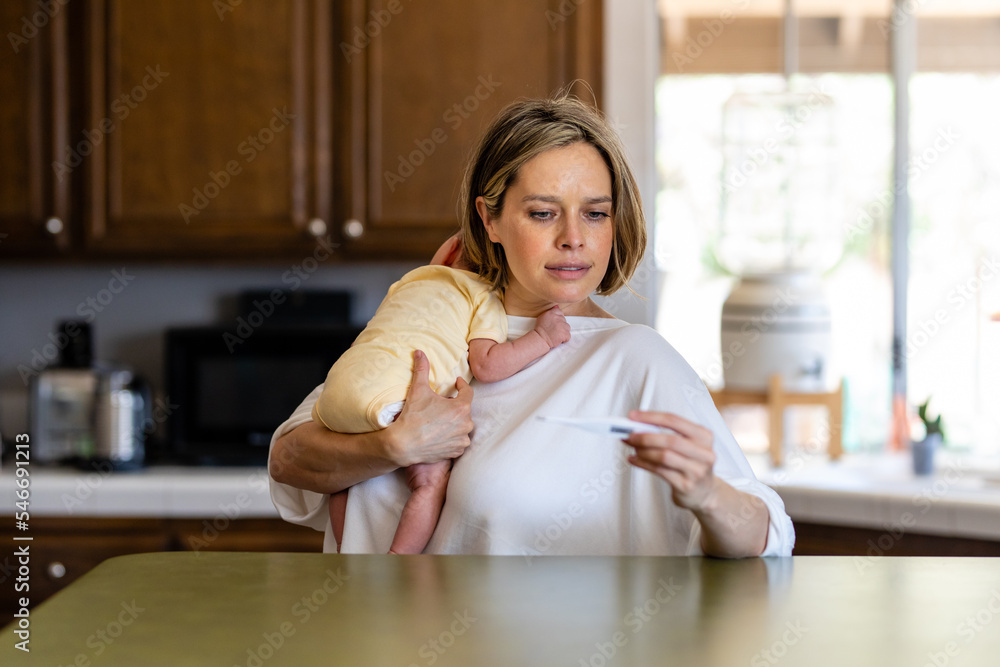 Mother Reads The Temperature On A Thermometer While Holding Infant Mother Reads The Temperature On A Thermometer While Holding Infant