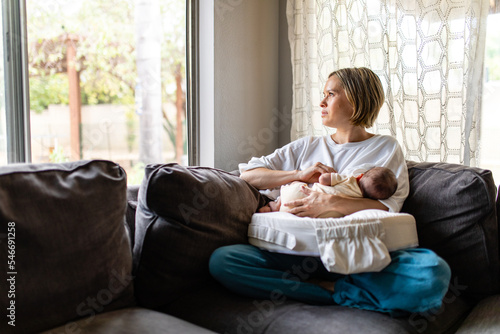 Mother Looks Solemnly Out The Window While Breastfeeding Infant photo