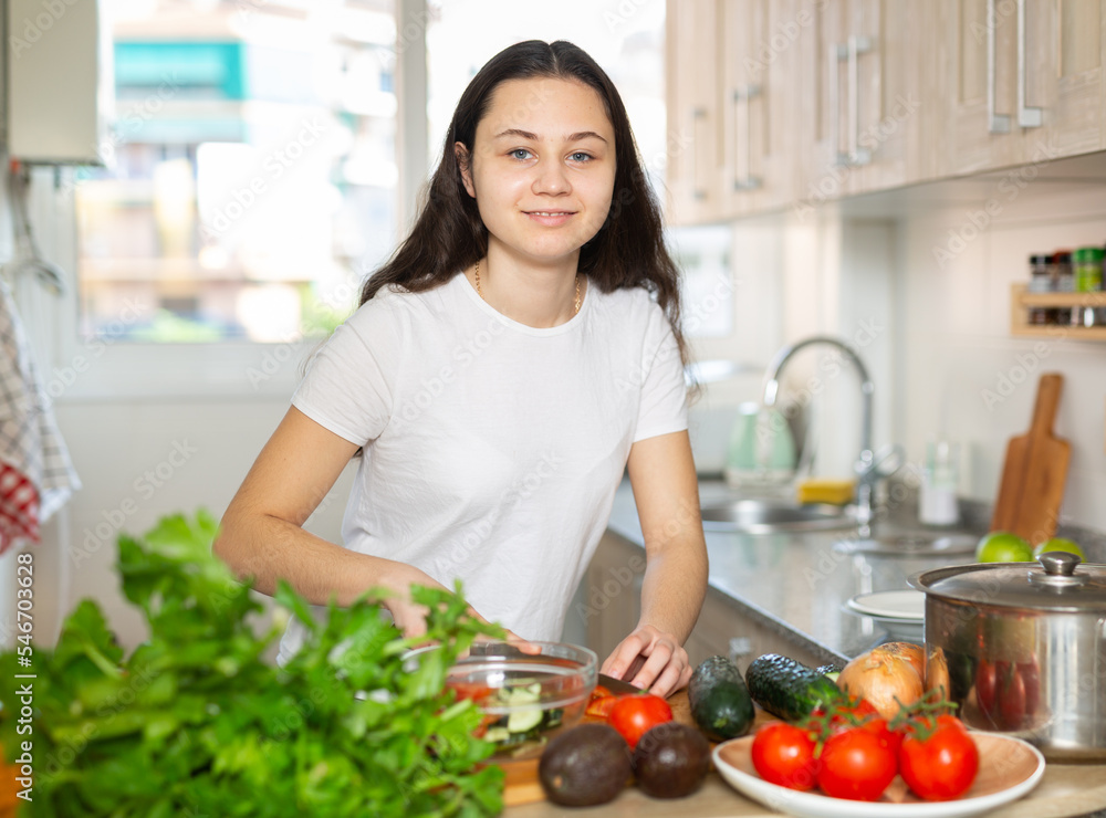 Beautiful positive young woman preparing vegetable salad in the kitchen