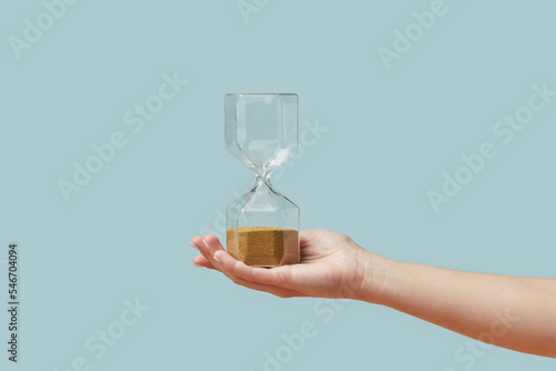 Hourglass with golden sand in woman's hand.
