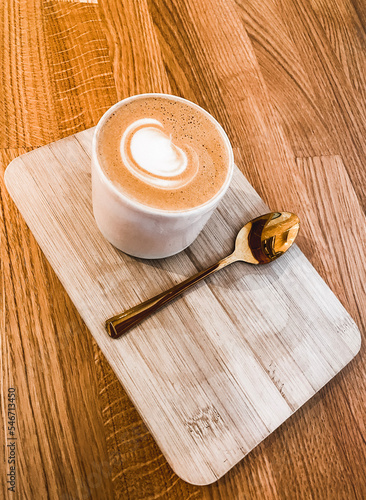 cup of coffee with latte art on wooden board and a golden spoon next to it, a flat white with a golden spoon, a cafe latte with a wooden background, latte macchiato high angle shot, cappucino 