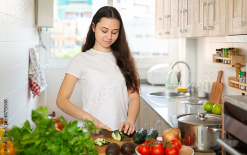 Young woman maintaining healthy lifestyle making fresh vegetable salad at kitchen