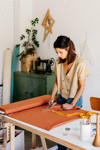 A standing woman cuts a piece of cloth on the table. photo