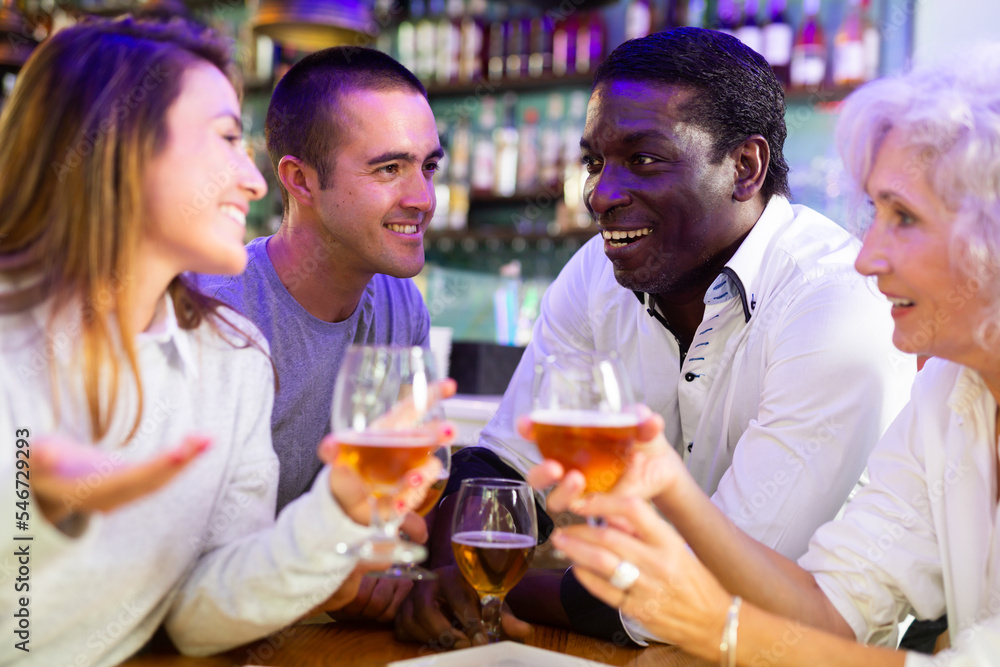 International group of glad cheerful people toasting with beer, having fun at party in beer pub. Focus on young man