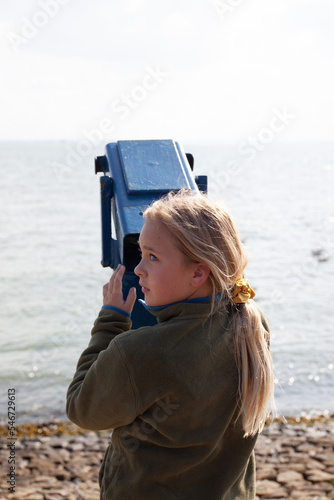 Girl looks whistfully along the shore. She is holding a binocular. photo