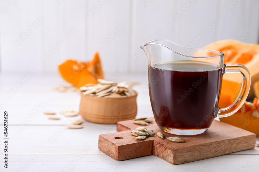 Fresh pumpkin seed oil in glass pitcher on white wooden table. Space for text Fresh pumpkin seed oil in glass pitcher on white wooden table. Space for text
