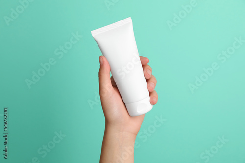 Woman holding tube of face cream on turquoise background, closeup