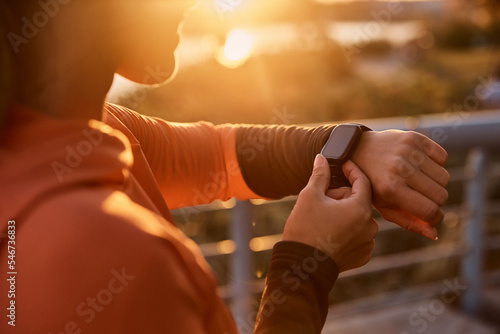 Close up of athletic woman measuring her heart rate on smartwatch at sunset.