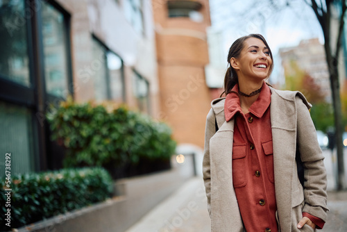 Young happy woman walking on city street and looking away.
