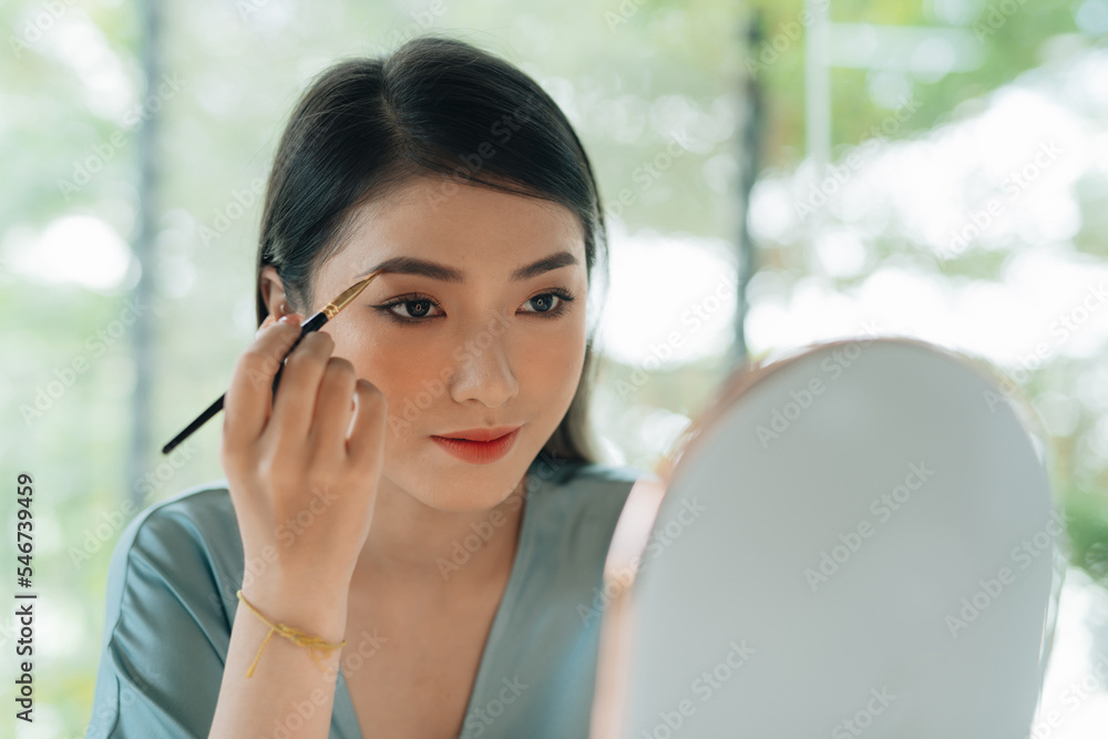 Young woman applying makeup drawing eyebrow with brush Young woman applying makeup drawing eyebrow with brush