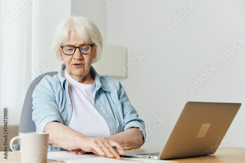 a business-like elderly lady works from home on a laptop at her desk and looks attentively while doing work